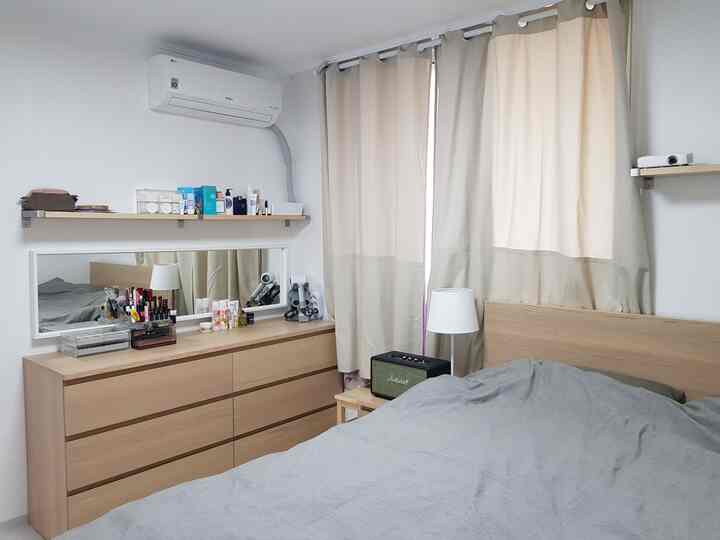 ナチュラルな木目調とグレーの寝具が配された寝室、イケアのチェストと壁棚、ベージュの遮光カーテンが配置された雰囲気のあるインテリア