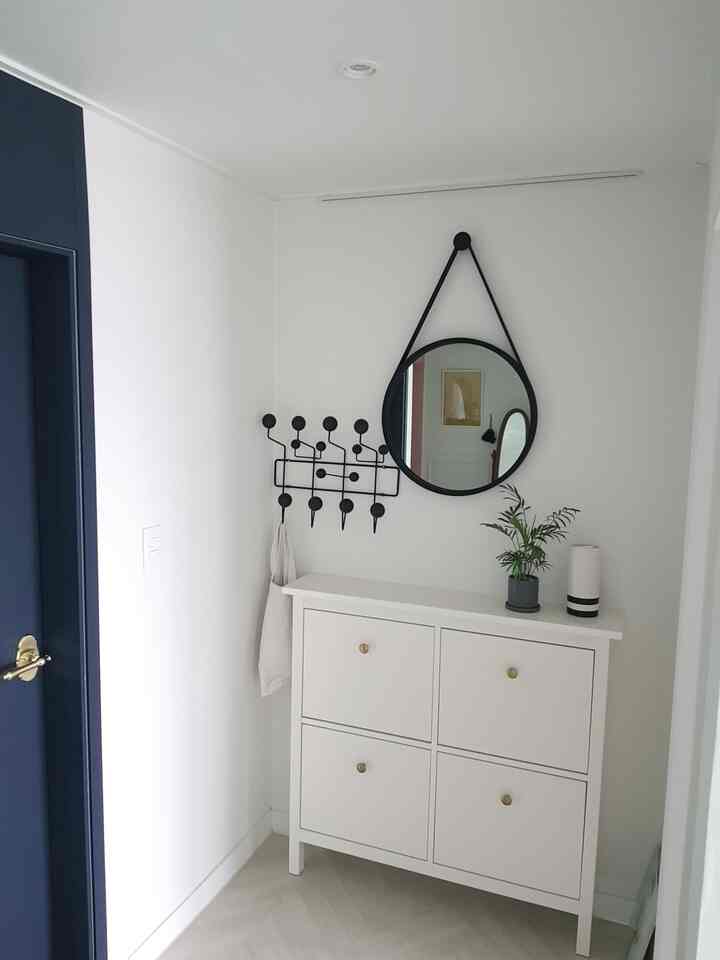 White-walled entrance space featuring a shoe cabinet, black strap circular mirror, and Hang It All hooks in a simple, clean layout