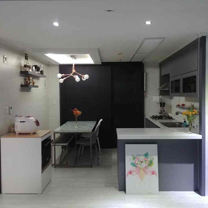 白い壁とグレーのキッチン家具が調和したモダンなキッチンとダイニング、フラミンゴの額縁とゴールドの照明が印象的な空間