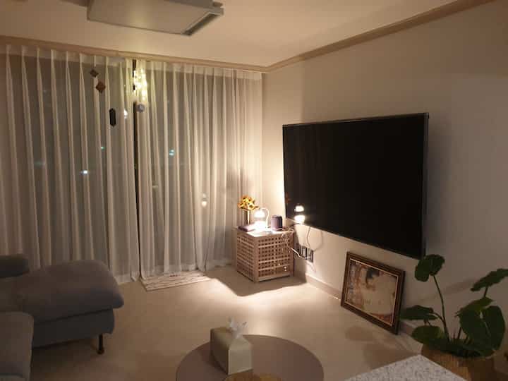 White-toned living room featuring curtains, gray sofa, wall-mounted TV, and natural decor creating a modern cozy atmosphere