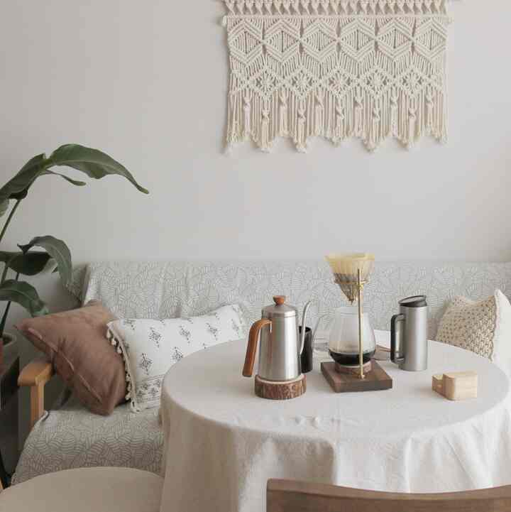ナチュラルな色調のリビングのおうちカフェ、マクラメの壁飾りとソファ、ドリップコーヒーセットが配置された雰囲気のある空間