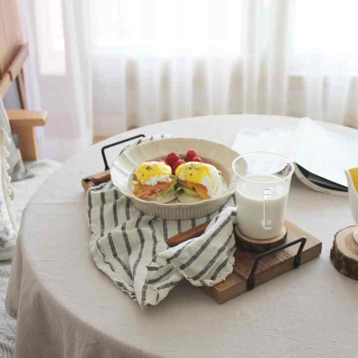 A cozy round dining table with soft white and wood tones, featuring a linen tablecloth and home brunch setup