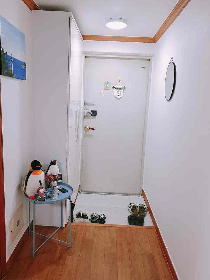 White and wood tone narrow entrance featuring shoes near door, small blue side table on left, round mirror on right wall, clean and tidy space