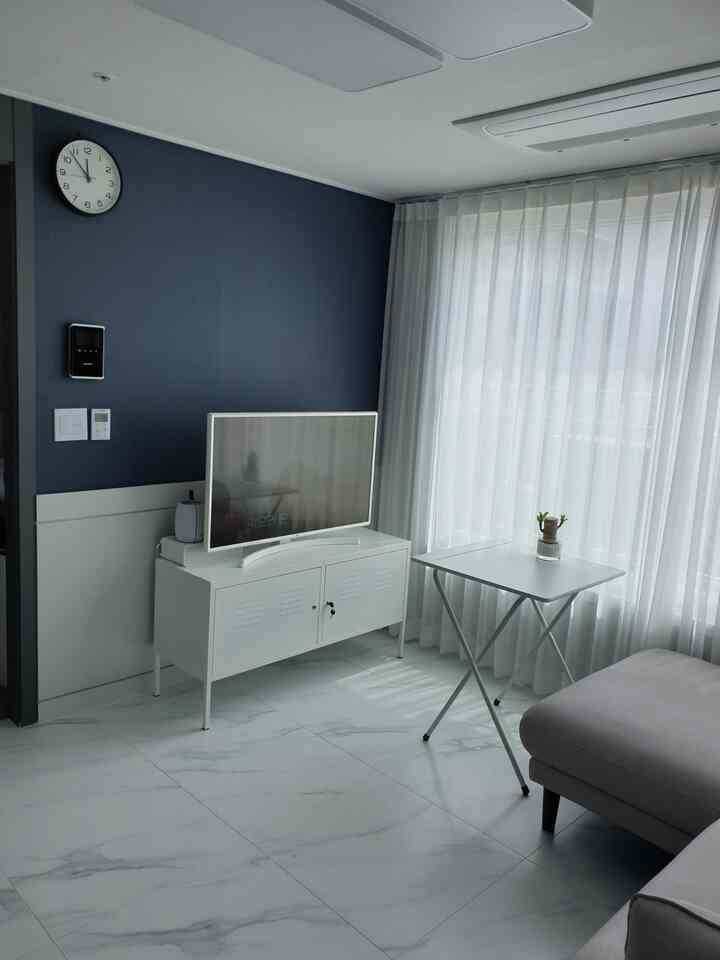 Living room in white and navy tones featuring a white TV stand, light gray sofa, and large sheer curtains, creating a modern and clean atmosphere
