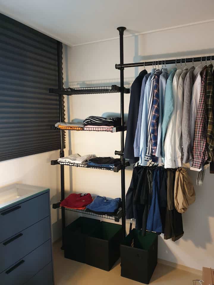 Compact walk-in closet featuring black hanger frame and storage boxes with neutral walls