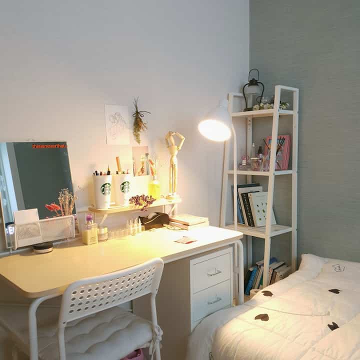 明るい白とベージュのトーンの小さな寝室、デスクと椅子、フロアランプが配置された自然な雰囲気のインテリア