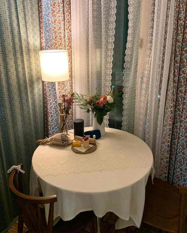 Vintage mood veranda space featuring a round table with lace curtains and floral decorations creating a cozy atmosphere.