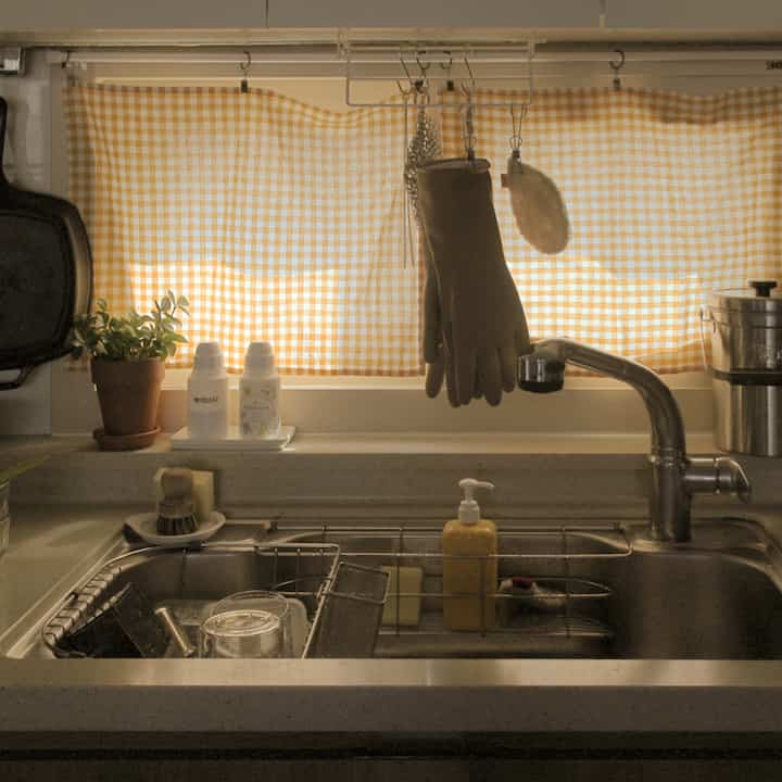 Warm beige-toned kitchen sink area with yellow checkered curtain, natural decor items, and retro atmosphere