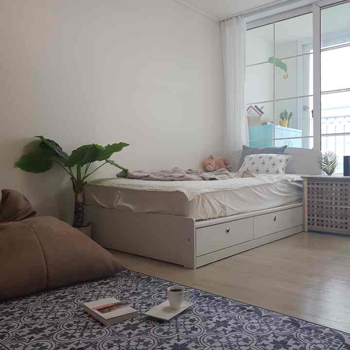 White toned bedroom featuring storage bed, bean bag, and patterned rug with a cozy natural atmosphere