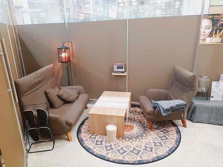 A cozy small waiting area in a single-person shop featuring brown sofas and armchairs arranged on a round Persian rug with natural tones