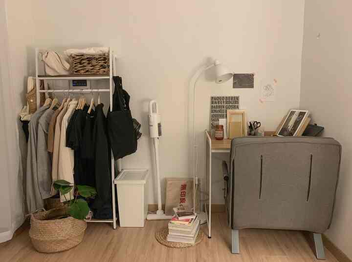 白とナチュラルカラーのワンルーム、クローゼット、デスク、アームチェア、フロアランプが配置された雰囲気のあるホームオフィス空間