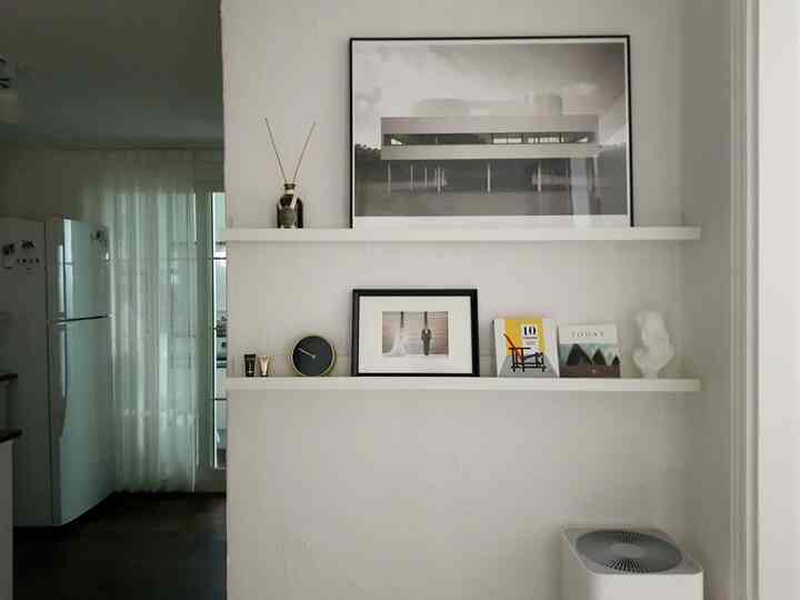A white-tone wall with shelves in a simple, tidy space decorated with framed art and various decor items