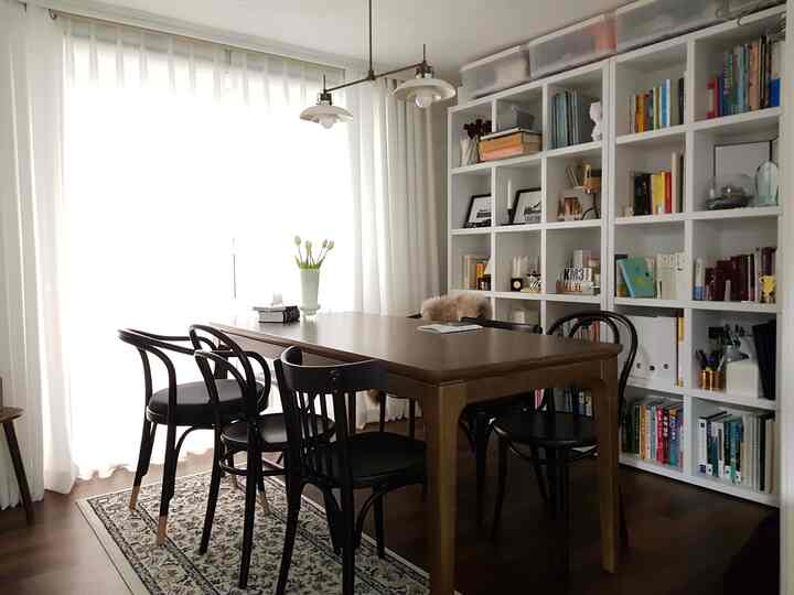 A white and wood-toned dining room featuring a large dining table, chairs, and bookshelves creating a cozy atmosphere