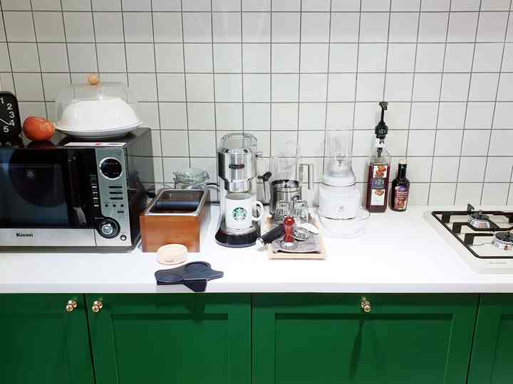 White tiled wall and green cabinets kitchen featuring coffee machine, blender, and other appliances in a compact functional space