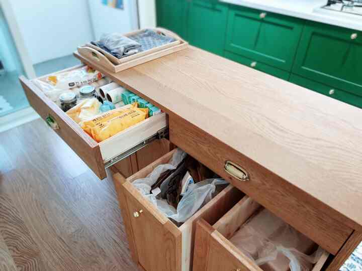 Natural wood tone storage cabinet and green kitchen cabinets in a clean, practical kitchen space