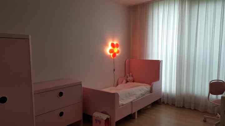 ピンク色調の子供部屋、ピンクのベッドとワードローブ、白いカーテンが配置された落ち着いた空間