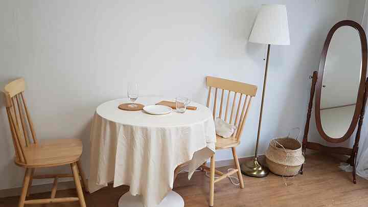 ナチュラルな色調の二人用円形ダイニングテーブルと椅子、フロアランプ、全身鏡が配置された落ち着いた空間