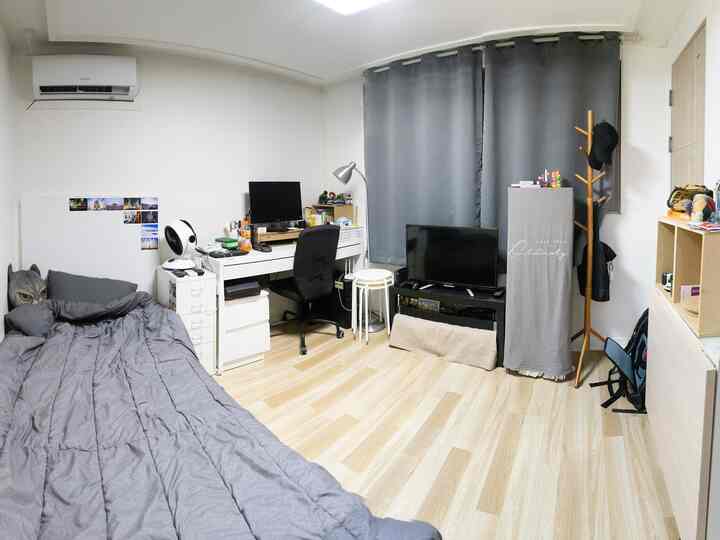 グレーのトーンとナチュラルウッドが調和した縦長の寝室、デスクとテレビ、遮光カーテンが整然と配置された空間