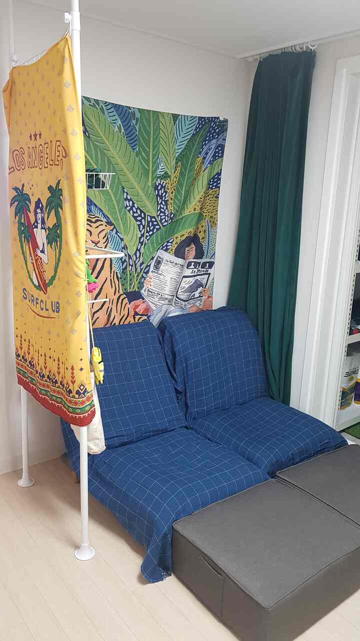 Natural toned small game room featuring blue floor sofas and green velvet blackout curtains with colorful wall tapestry