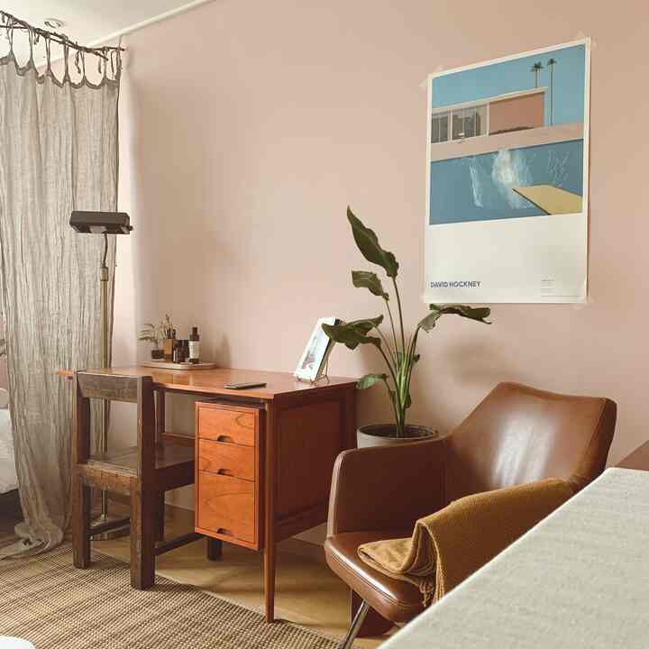落ち着いたピンクの壁のワンルーム、木製デスクとブラウンレザーのアームチェアが置かれた雰囲気のあるインテリア