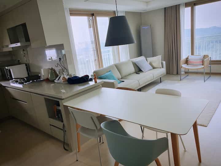 グレーのモノトーンとウッドトーンが調和した北欧スタイルの2ベイリビング空間、ペンダントライトの下にダイニングテーブルとソファが配置された温かみのあるインテリア