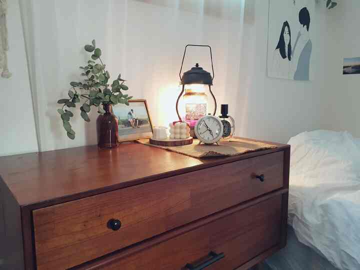 白い壁と寝具のある寝室、茶色のドレッサーの上に照明と装飾品が配置されたナチュラルスタイルのインテリア