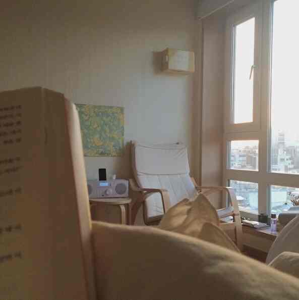 Living room with white walls and natural wood furniture, featuring cozy armchair and window seat creating a warm, simple atmosphere