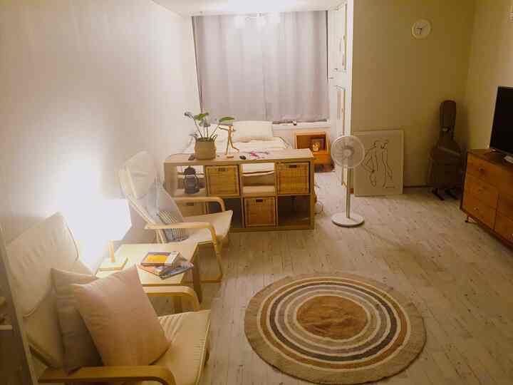 Warm beige natural wood tone studio apartment with armchairs and table lamp creating cozy atmosphere
