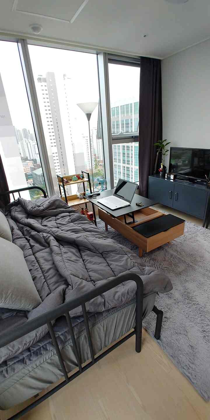 チャコールとグレーのトーンが特徴の狭いワンルーム、ソファベッドとテレビ台、ホームオフィスが配置されたモダンなインテリア