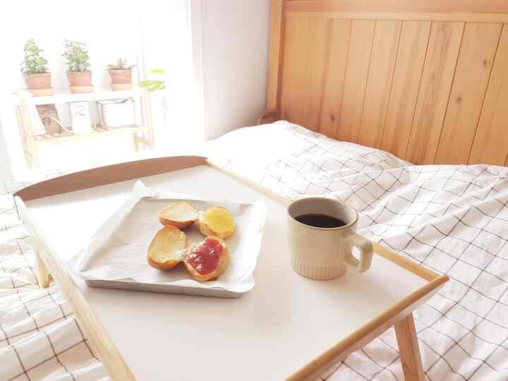 Natural wood tones and white bedroom featuring a tray on the bed with toasted morning rolls and coffee creating a cozy breakfast scene