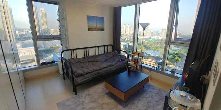 White and natural tone small studio bedroom featuring sofa bed, coffee table, and large windows providing an open atmosphere