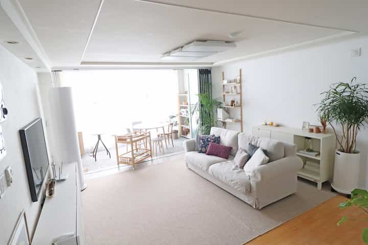 明るいホワイトの壁と木製キャビネット、ベージュのファブリックソファが配置されたナチュラルなリビング