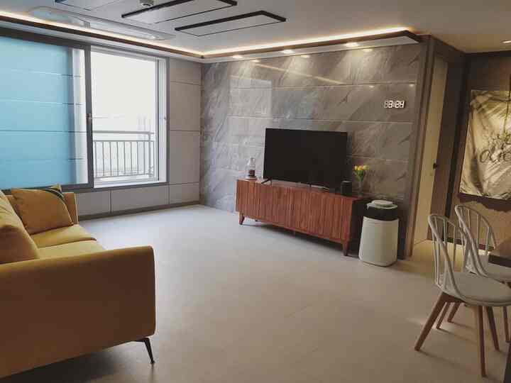 Bright white floor living room with brown TV stand and centered yellow sofa, creating a clean and modern atmosphere