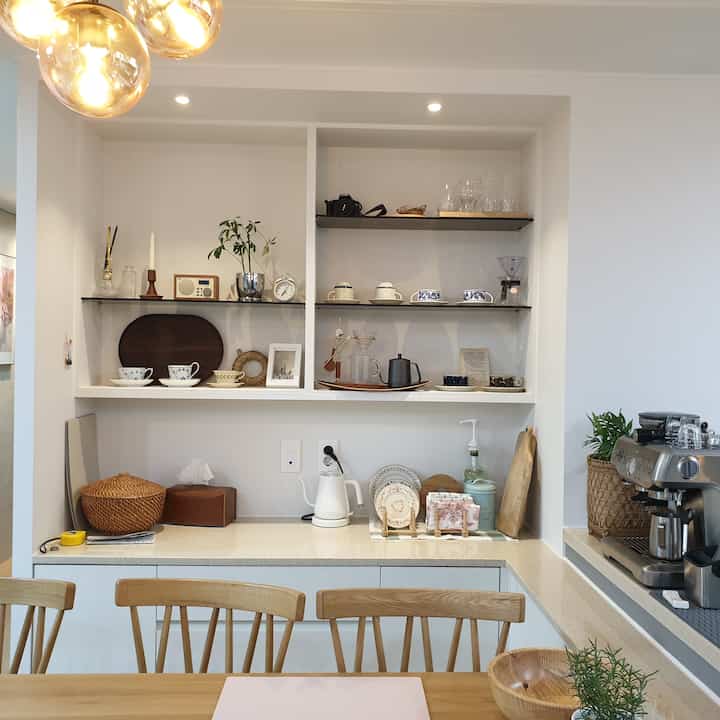 White-toned kitchen with wood dining table, coffee machine, and teacups arranged in a modern natural home cafe space