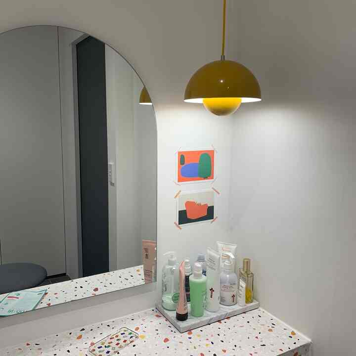Minimal and clean vanity space with white walls and terrazzo countertop, accented by a mustard yellow pendant light