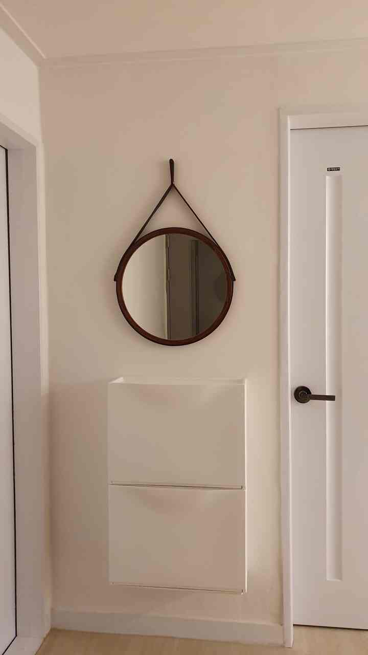 暖かいホワイトトーンの玄関スペース、壁に掛けられた丸いストラップミラーとモダンなホワイトのシューズラックが配置された実用的な空間