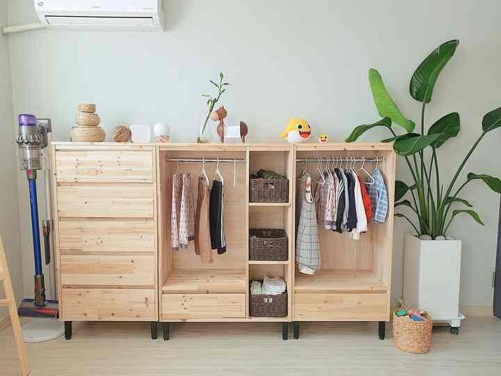 Bright natural wood-tone kids' room featuring wooden wardrobes with rattan storage baskets, baby clothes, and toys in tidy arrangement