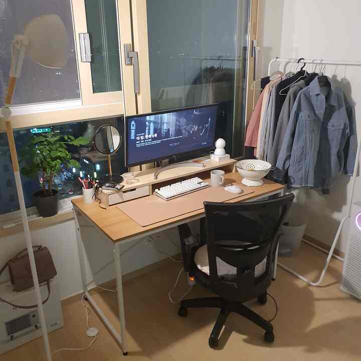 Natural wood tone and white studio home office featuring a monitor stand, floor lamp, and clothing rack, creating a clean workspace