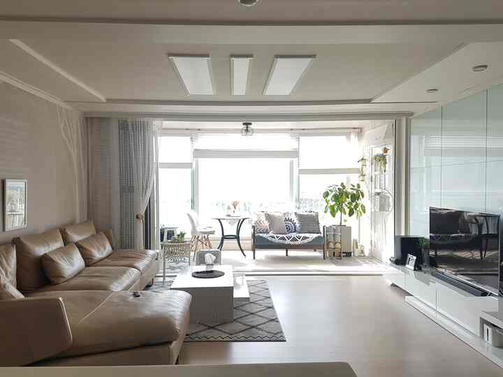 White and beige toned living room and veranda featuring modern sofa and round table with bright, open atmosphere