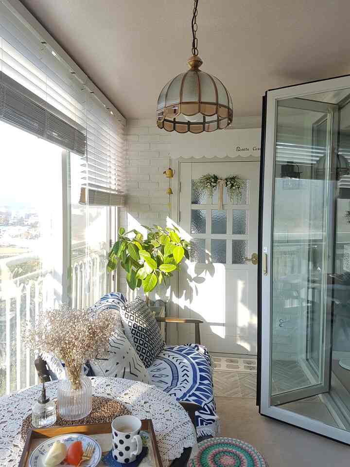 Bright white-toned veranda space featuring a blue patterned sofa, folding door, and dining table creating a cozy home cafe atmosphere