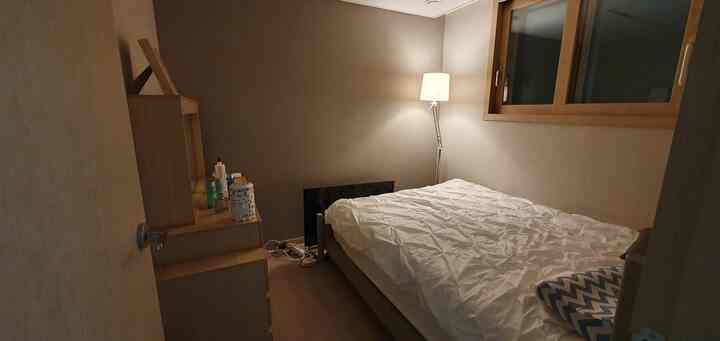 ベージュの壁と木目調家具が配置された落ち着いた寝室、ベッドとフロアランプで暖かみのある雰囲気のインテリア