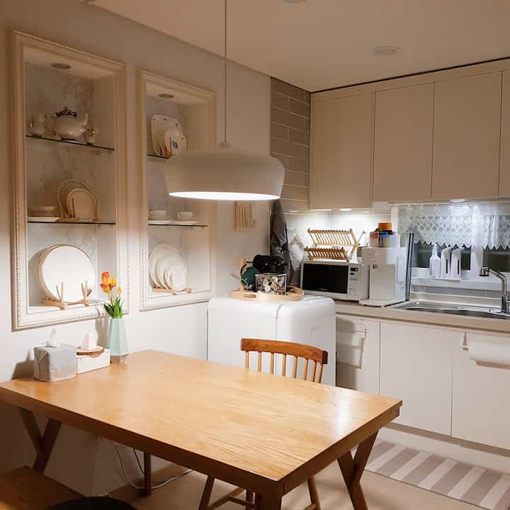 Natural-toned L-shaped kitchen featuring wood dining table and chairs with pendant lighting in a clean space