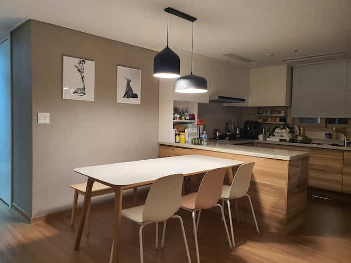 Natural wood tones and white kitchen and dining room featuring a simple dining table, chairs, and pendant lights creating a modern atmosphere