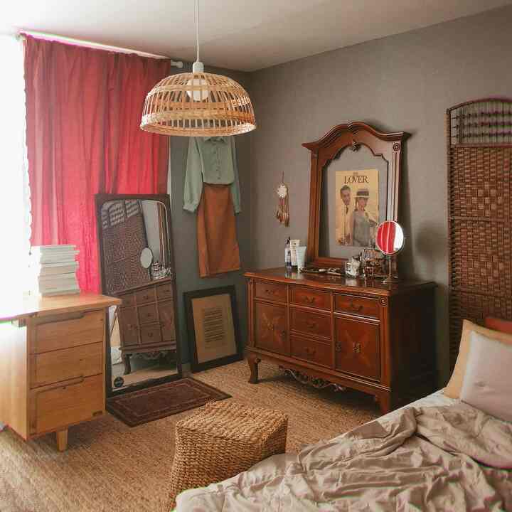 暖かいブラウンと赤のトーンのワンルーム寝室、木製の化粧台とカーテン、快適な寝具が配置された雰囲気のあるインテリア