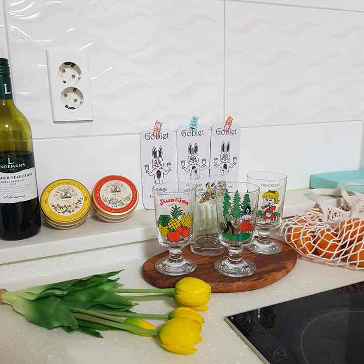 Bright kitchen countertop featuring a wooden tray with playful illustrated glass cups and yellow tulips arranged nearby