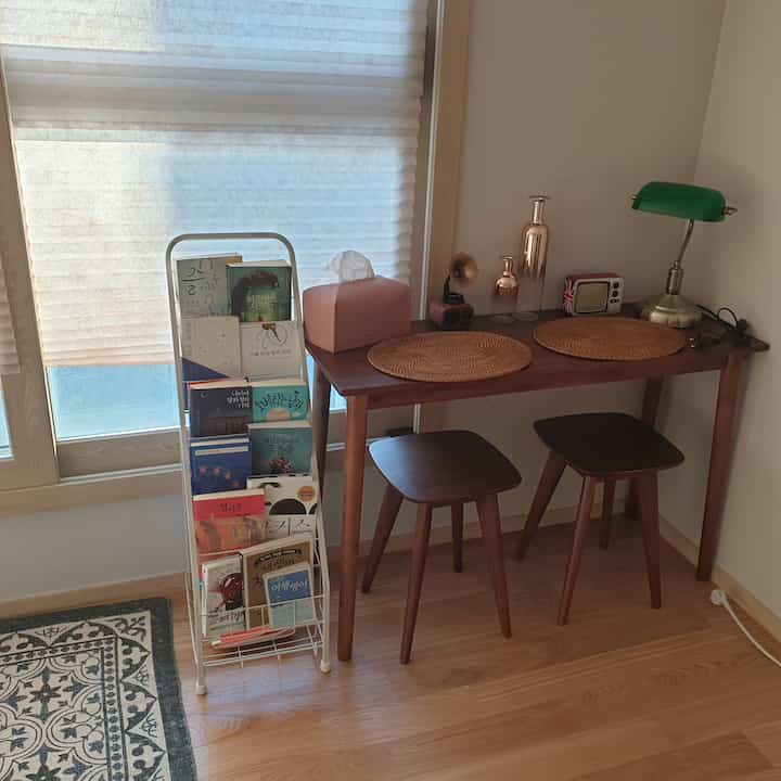A small home cafe space with white and wood tones, featuring a wooden dining table and bookshelf creating a cozy atmosphere
