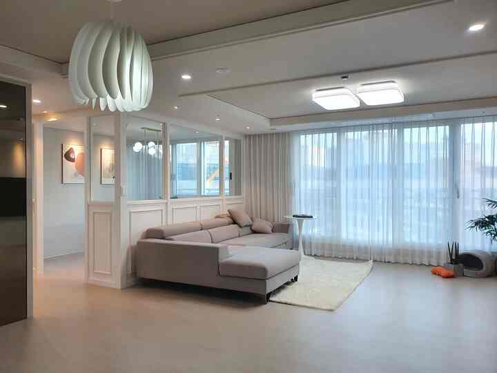White and light brown toned living room featuring a large gray sofa, pendant light, and a pet area with a modern aesthetic