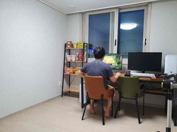 Bright white and wood tone small room game setup featuring desk, chairs, and metal shelving with remote work and gaming purpose