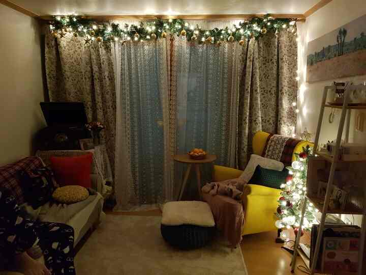 Cozy living room with warm lighting and Christmas decorations, featuring a yellow armchair and floor stool