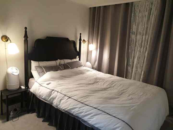 Black and white toned bedroom featuring a large bed, nightstand with air purifier, wall sconces, creating a calm and neat atmosphere